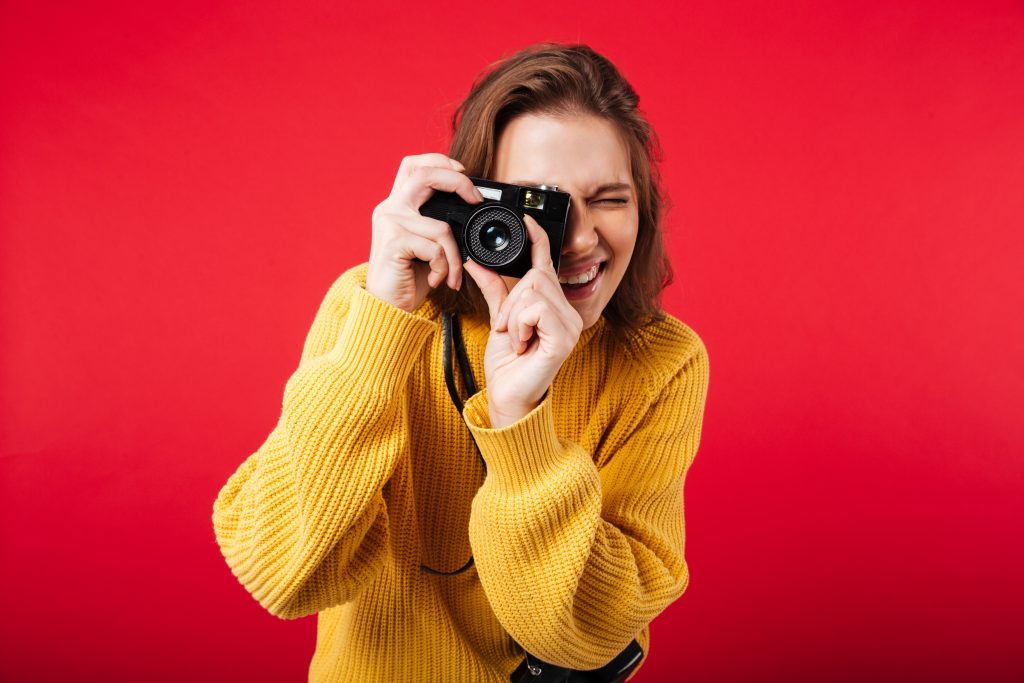 Portrait of a young woman taking a picture with a vintage camera isolated over pink background
