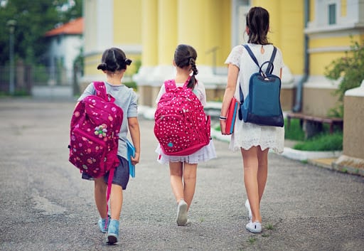 Three young girls are walking in the school yard at first day at school