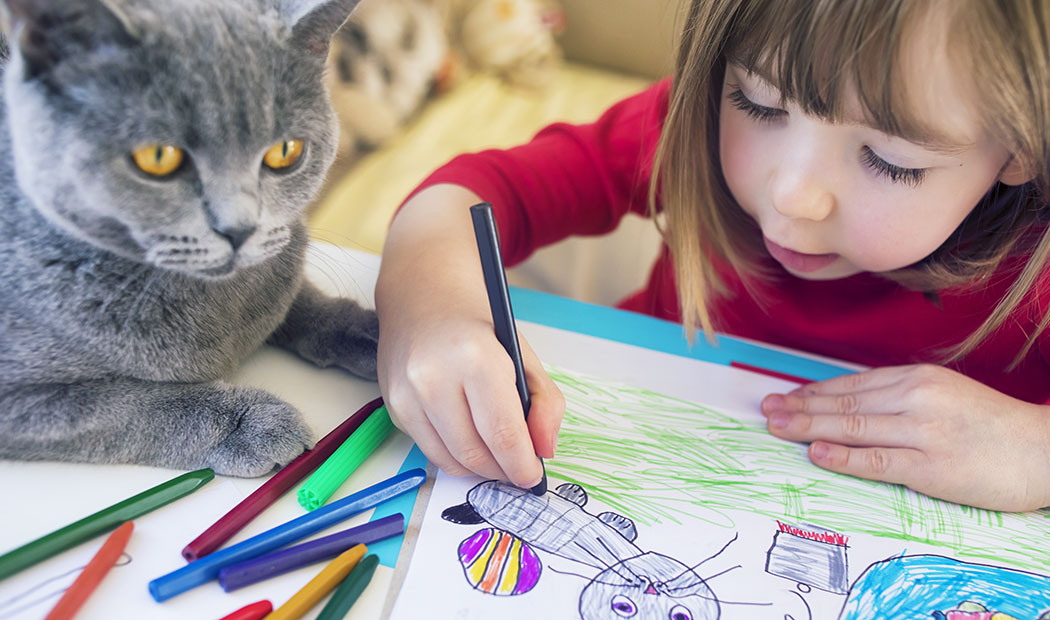 Cute child drawing at home. Kitty next to him.